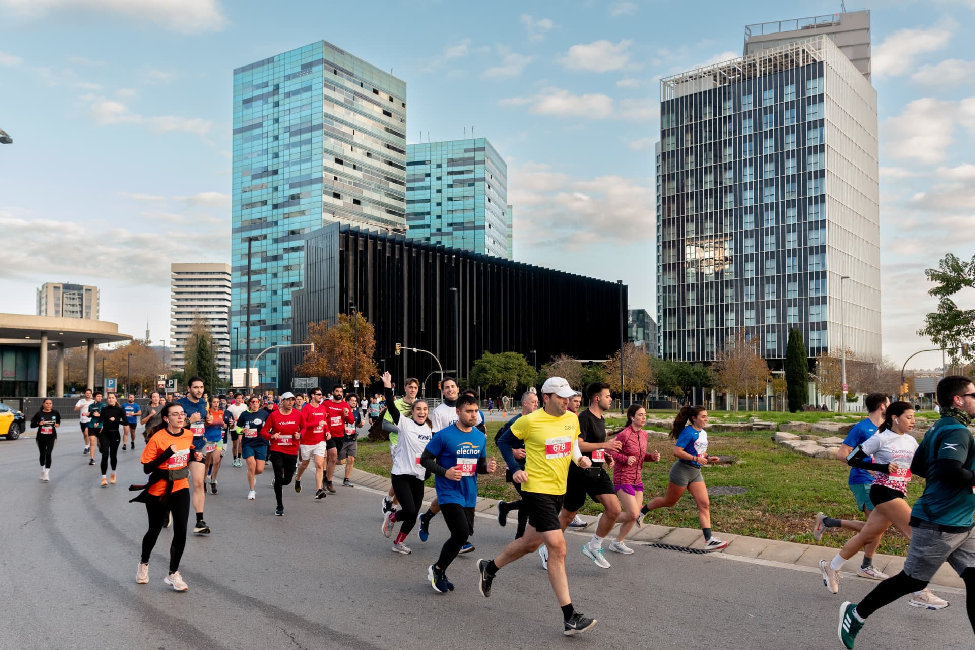 Cursa de les Empreses de Barcelona — Participantes corriendo por la ciudad con los edificios de oficinas al fondo.